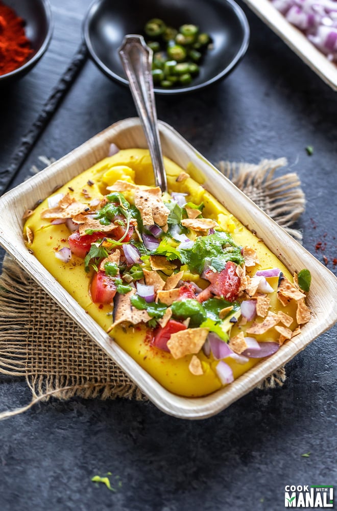 moong dal chaat served with a spoon in a rectangular bowl topped with onions, cilantro, tomatoes