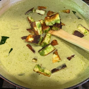 fried paneer pieces being added to a curry in a pan