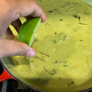 hand squeezing lime into a curry in a pan
