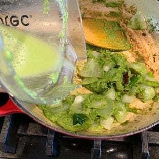 water being added to a pan with onions coated with green color paste