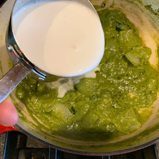 coconut milk being added to a green color curry