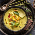 paneer lemongrass coconut curry served in a black bowl with stalks of lemongrass placed in the background and garnished with lime wedge
