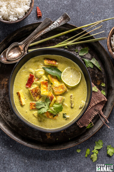 paneer lemongrass coconut curry served in a black bowl with stalks of lemongrass placed in the background and garnished with lime wedge
