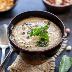 peanut chutney served in a wooden bowl topped with mustard seeds, curry leaves with a bowl of raw peanuts and chana dal in the background