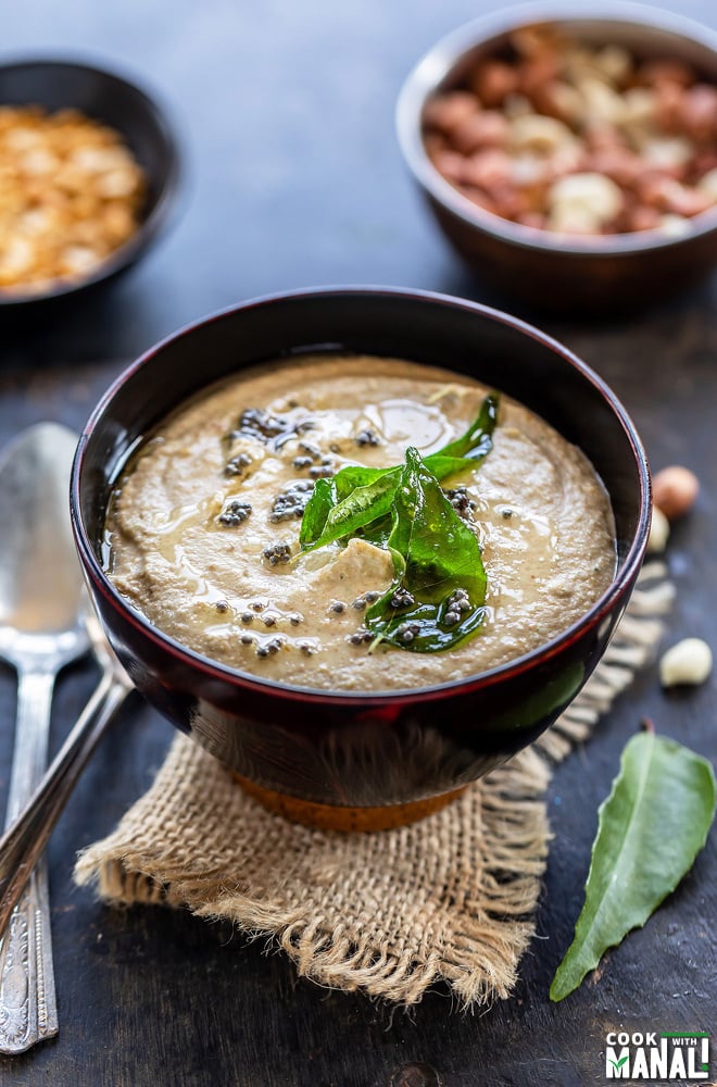 peanut chutney served in a wooden bowl topped with mustard seeds, curry leaves with a bowl of raw peanuts and chana dal in the background