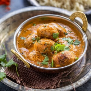 dum aloo served in a copper kadai garnished with cilantro with a plate of rice in the background