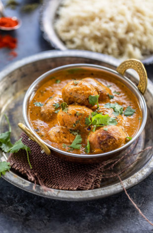 dum aloo served in a copper kadai garnished with cilantro with a plate of rice in the background