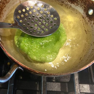 dough puffing up in oil and being pressed by a spatula