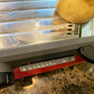 potato being sliced using a mandoline slicer