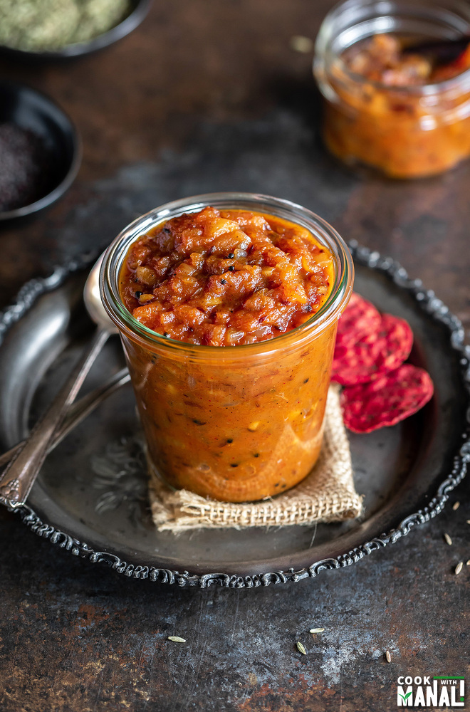 apple chutney in a glass jar with crackers placed on the side and some spices in the background