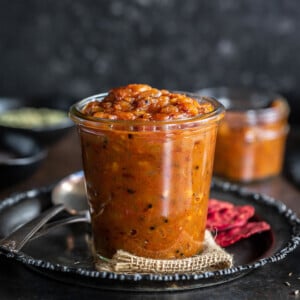 apple chutney in a glass jar with crackers placed on the side and some spices in the background