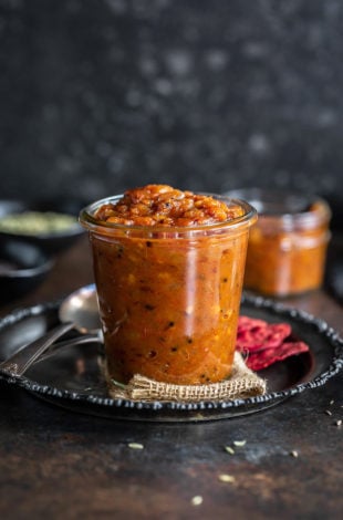 apple chutney in a glass jar with crackers placed on the side and some spices in the background