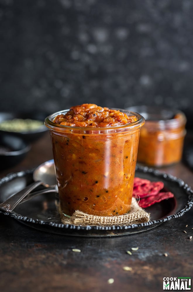 apple chutney in a glass jar with crackers placed on the side and some spices in the background