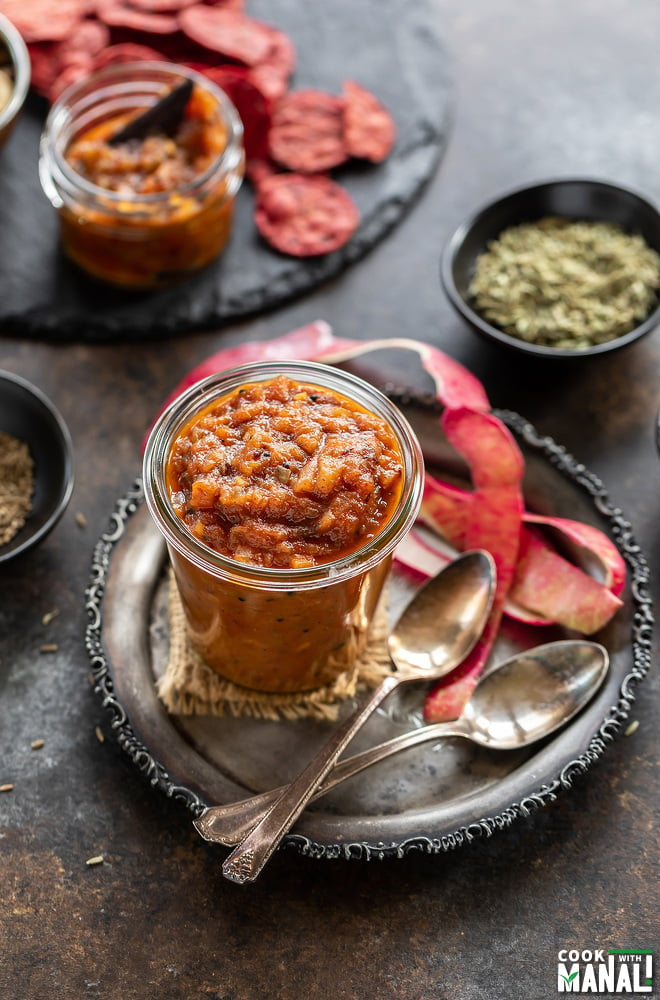 apple chutney in a glass jar with apple peel placed on the side and few spice bowls in the background