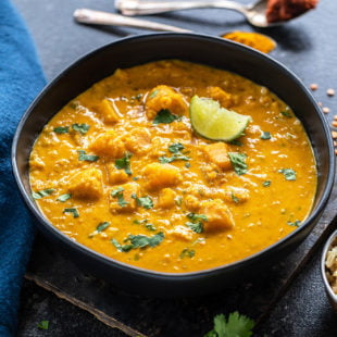 bowl of squash curry garnished with cilantro and few twigs of cilantro and squeezed lime placed on the side