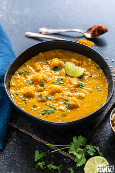 bowl of squash curry garnished with cilantro and few twigs of cilantro and squeezed lime placed on the side