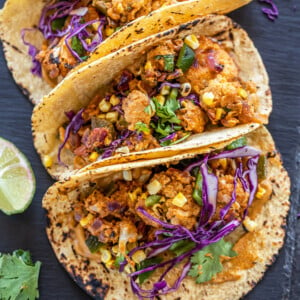 3 tacos filled with cauliflower, topped with cilantro and arranged on a black board