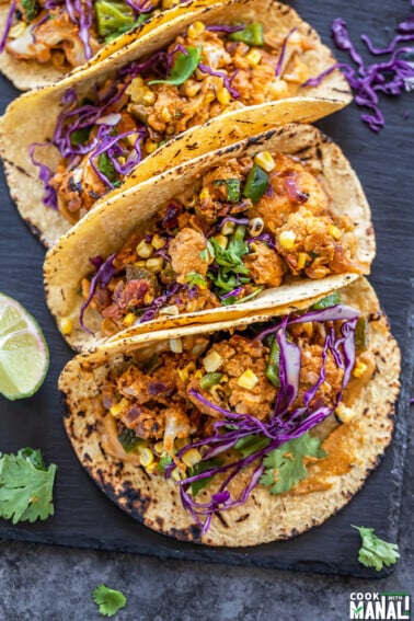 3 tacos filled with cauliflower, topped with cilantro and arranged on a black board