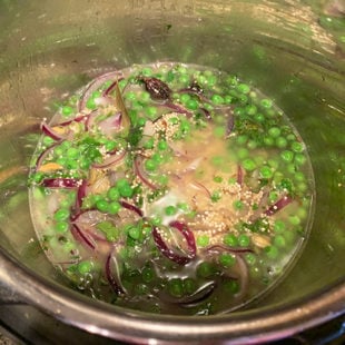 quinoa, green peas, cilantro and spices mixed together in a pot along with water