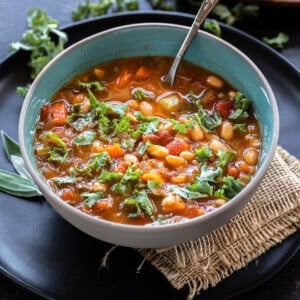 bowl of soup with kale, white beans served with a spoon and lots of chopped kale placed in the background