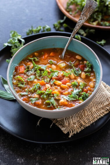 bowl of soup with kale, white beans served with a spoon and lots of chopped kale placed in the background