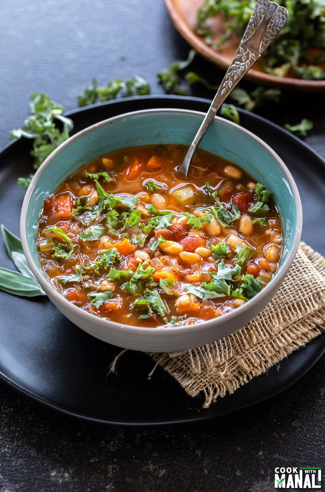 bowl of soup with kale, white beans served with a spoon and lots of chopped kale placed in the background