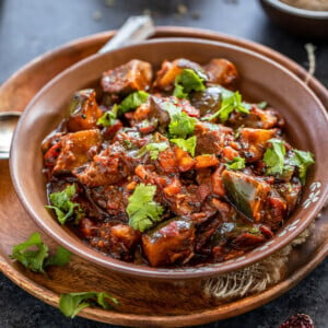 eggplant curry served in a brown bowl, garnished with cilantro and bowls of spices placed in the background