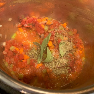 crushed tomatoes with sage leaves and other dried herbs in a pot