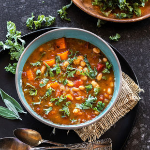 bowl of soup with white beans, kale and spoons placed on the side