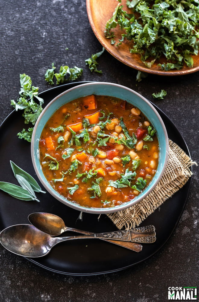 bowl of soup with white beans, kale, tomato and lots of chopped kale placed in the background