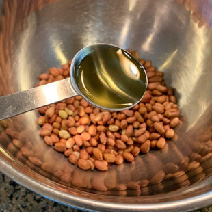 oil being added to a bowl of peanuts