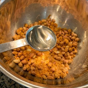 water being added to a bowl of peanuts and spices