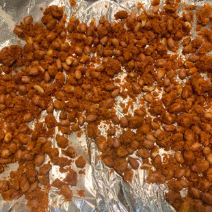 peanuts coated with spices on a baking sheet lined with aluminum foil