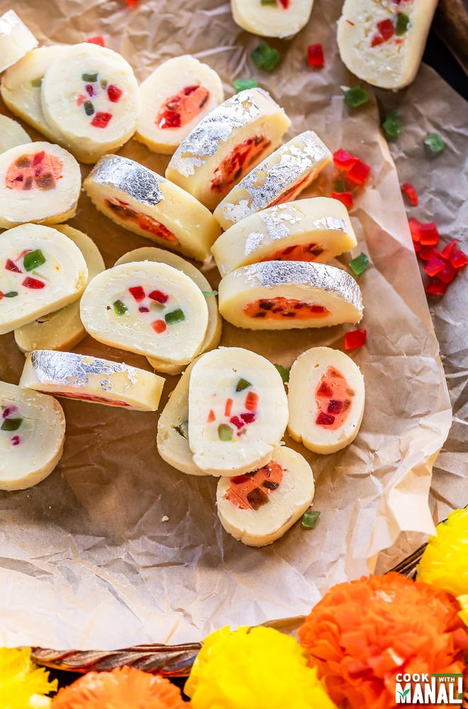 plate of sliced burfi roll with some artificial flowers on sides