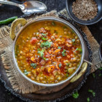 green lentils served in a copper kadai and garnished with cilantro and spices