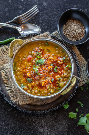 green lentils served in a copper kadai and garnished with cilantro and spices