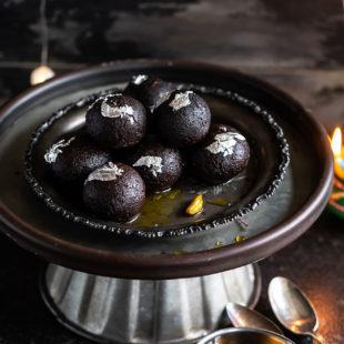 kala jamun arranged on an antique plate with some lights in the background