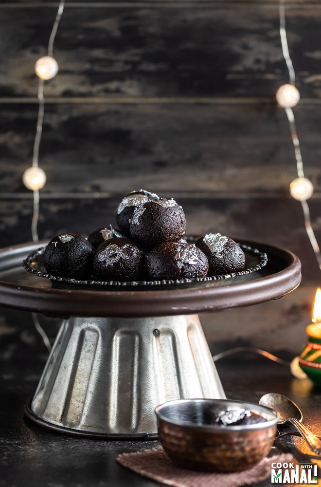 kala jamuns arranged in a plate and place of a cake stand with strings of lights in the background