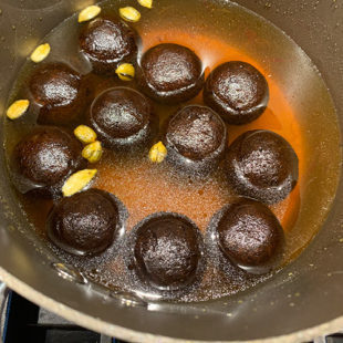 round dough balls dunked in sugar syrup in a pan