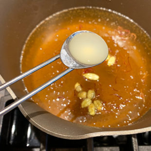 teaspoon of lemon juice being added to a pan of sugar syrup