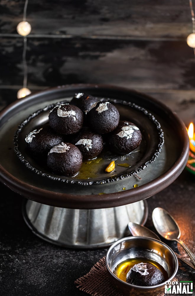 kala jamun arranged on an antique plate with some lights in the background