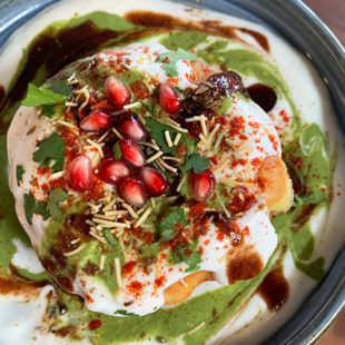 crisp fried ball of dough crushed open and filled with yogurt, chutney, topped with spices, cilantro, pomegranate
