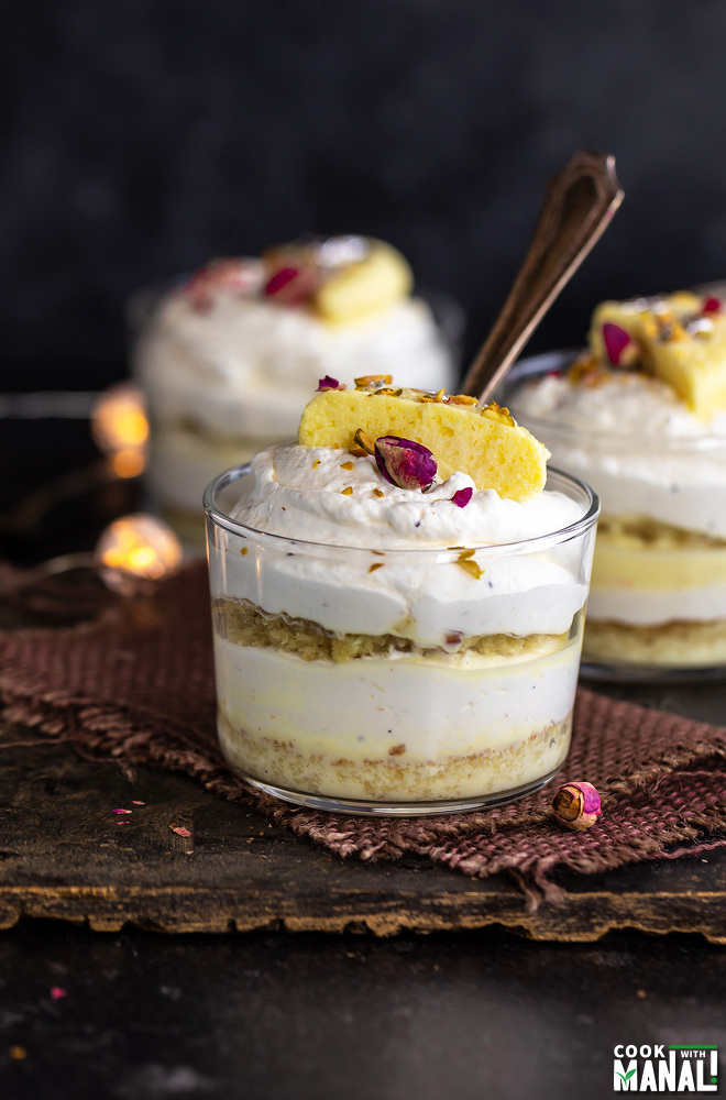 3 rasmalai cake jars placed on a board with lights in the background