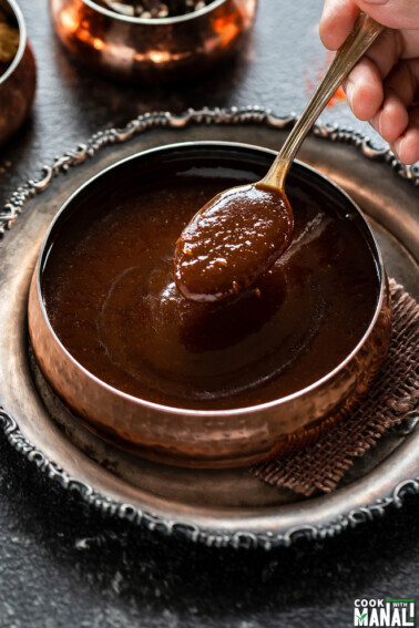 spoon inside a bowl of tamarind chutney served in a copper bowl