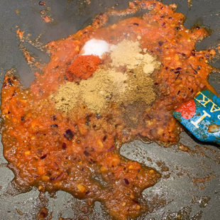 spices being added to a onion-tomato masala on a griddle