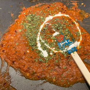 kasuri methi and cream drizzled on a onion tomato masala on a griddle