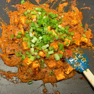 paneer and green onions with masala and spices on a griddle