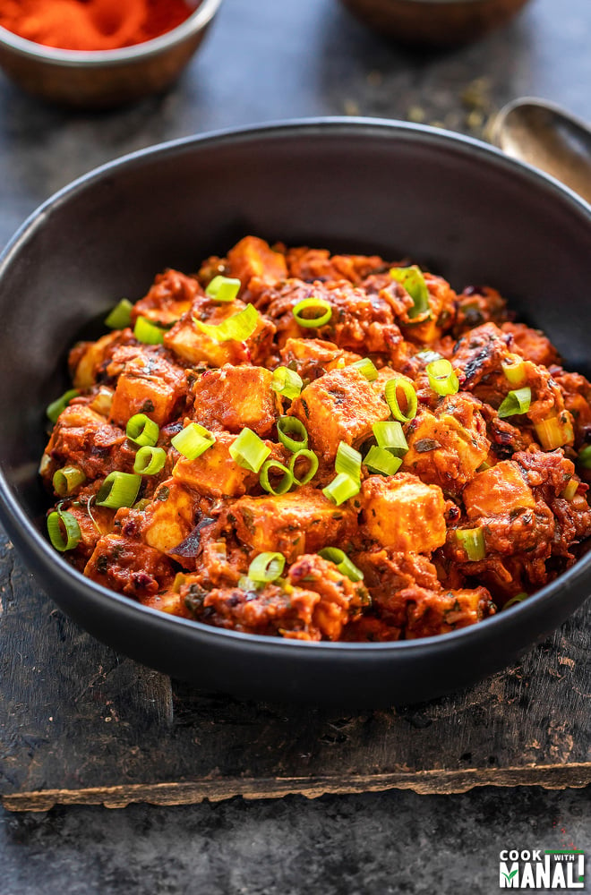 spiced paneer topped with green onions served in a black bowl