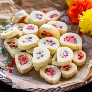 plate of burfi rolls with flowers placed on the side