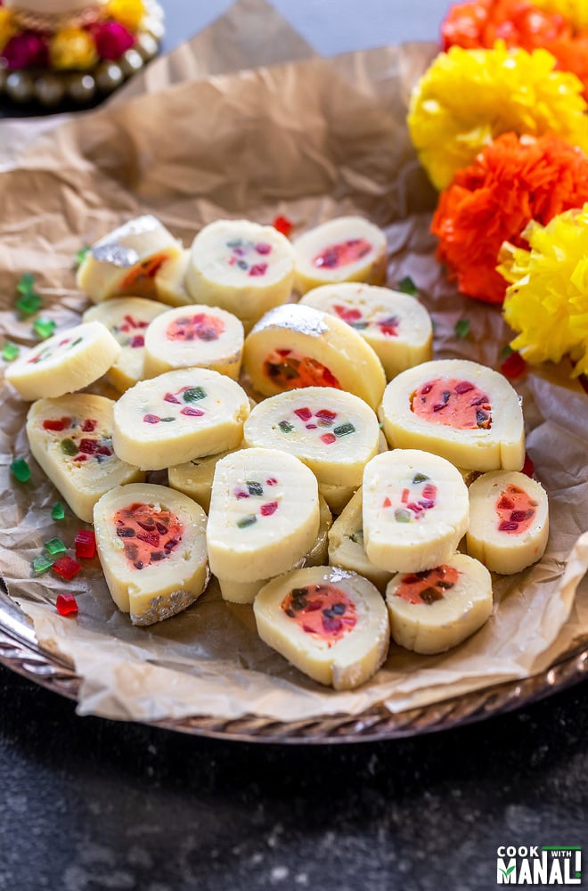 plate of burfi rolls with flowers placed on the side